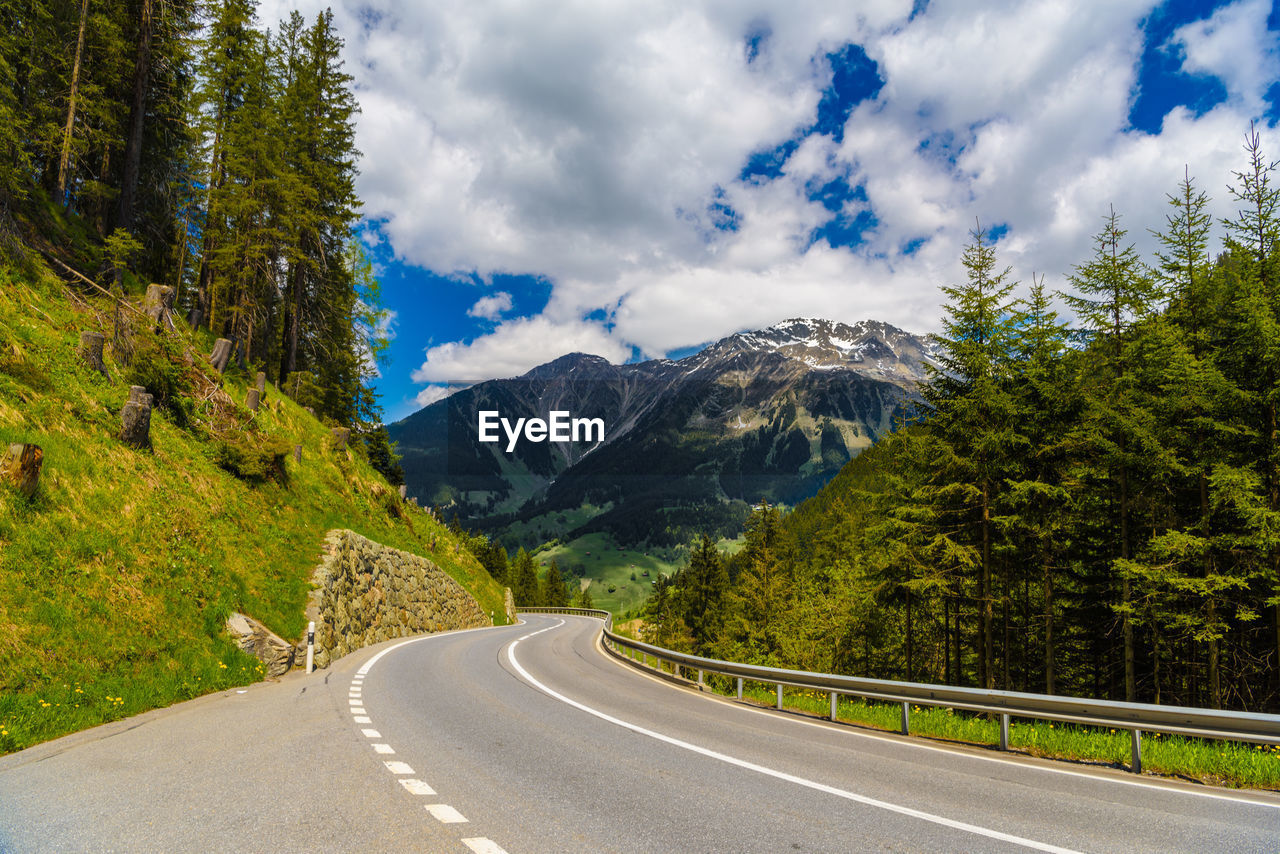 ROAD BY TREES AND MOUNTAINS AGAINST SKY