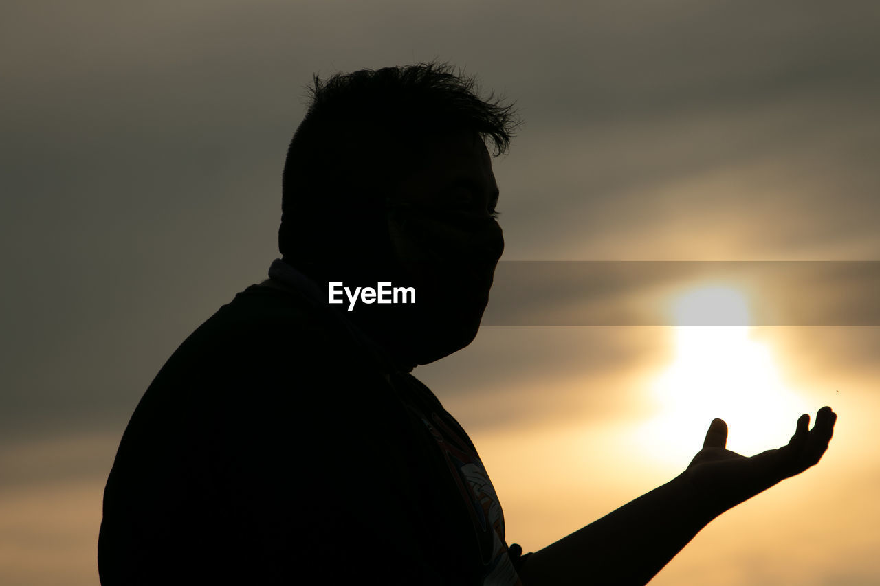 Man gesturing against sky during sunset