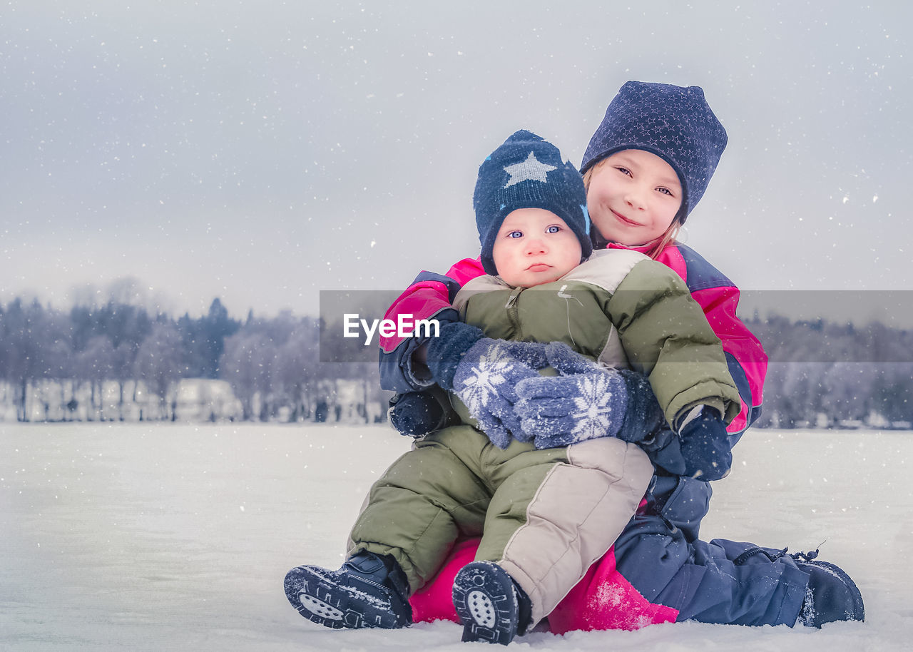 Portrait of siblings sitting on snow covered land