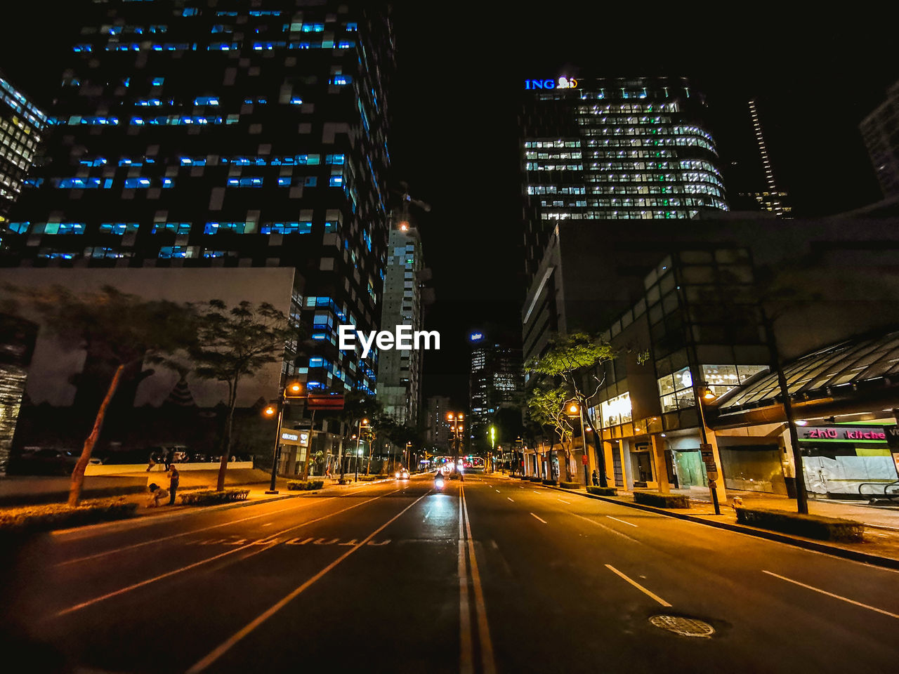 Illuminated street by buildings in city at night