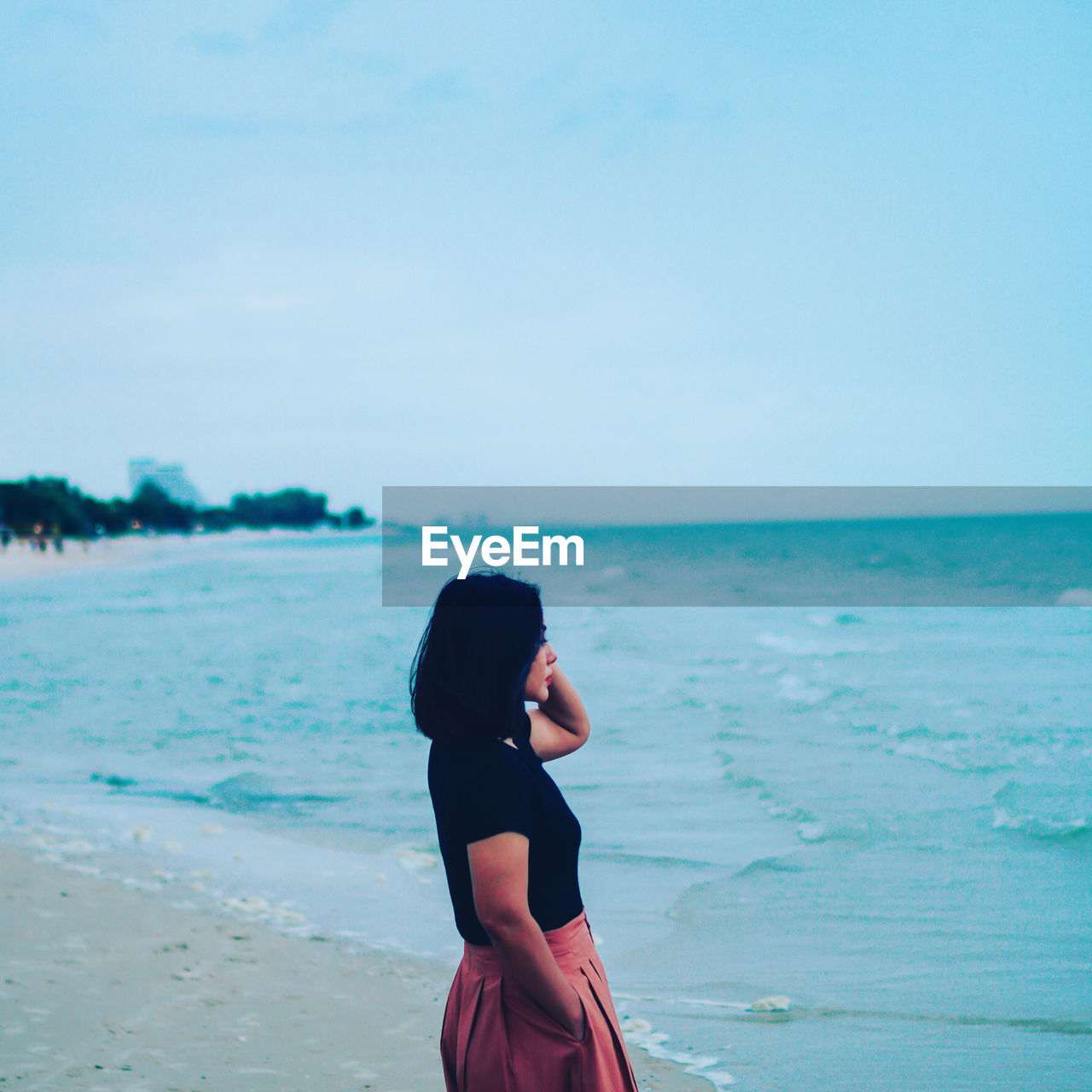 Side view of woman standing at beach against clear sky