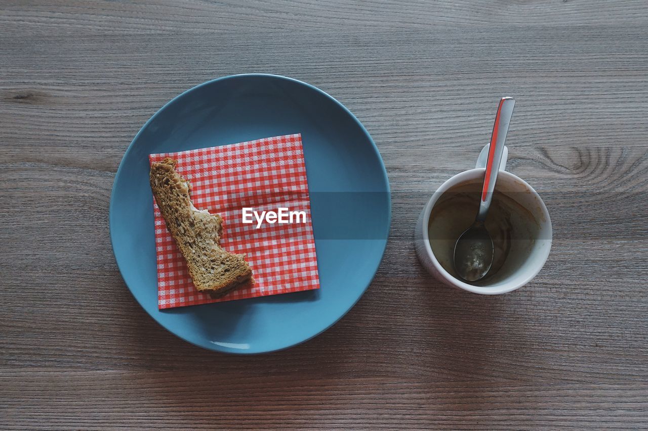 Directly above shot of eaten bread in plate by coffee cup on wooden table