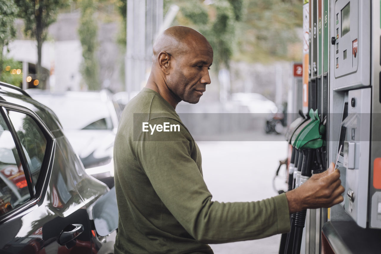 Side view of mature man doing payment through credit card while standing at gas station