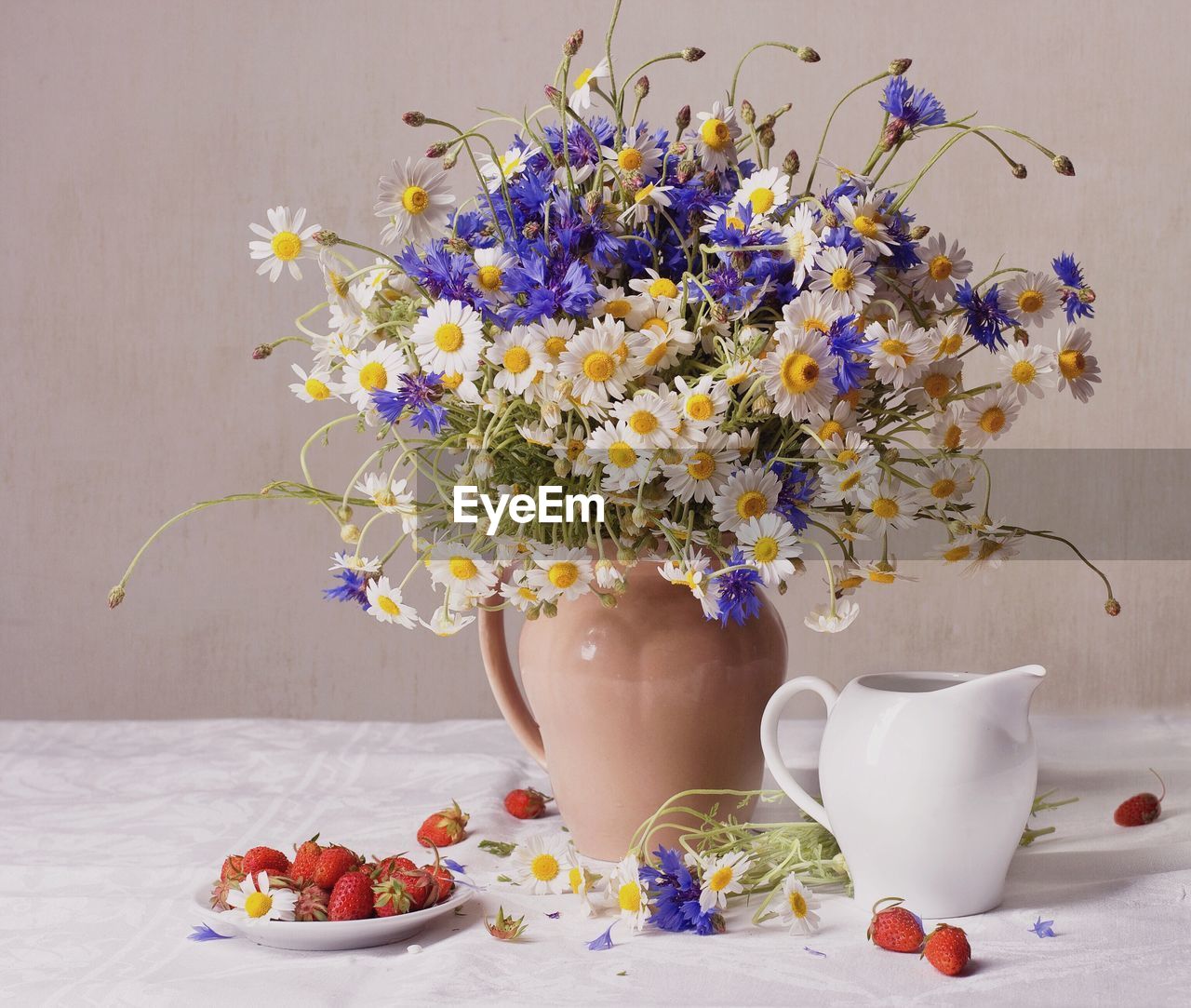 Flower vase with strawberries in plate on table against wall