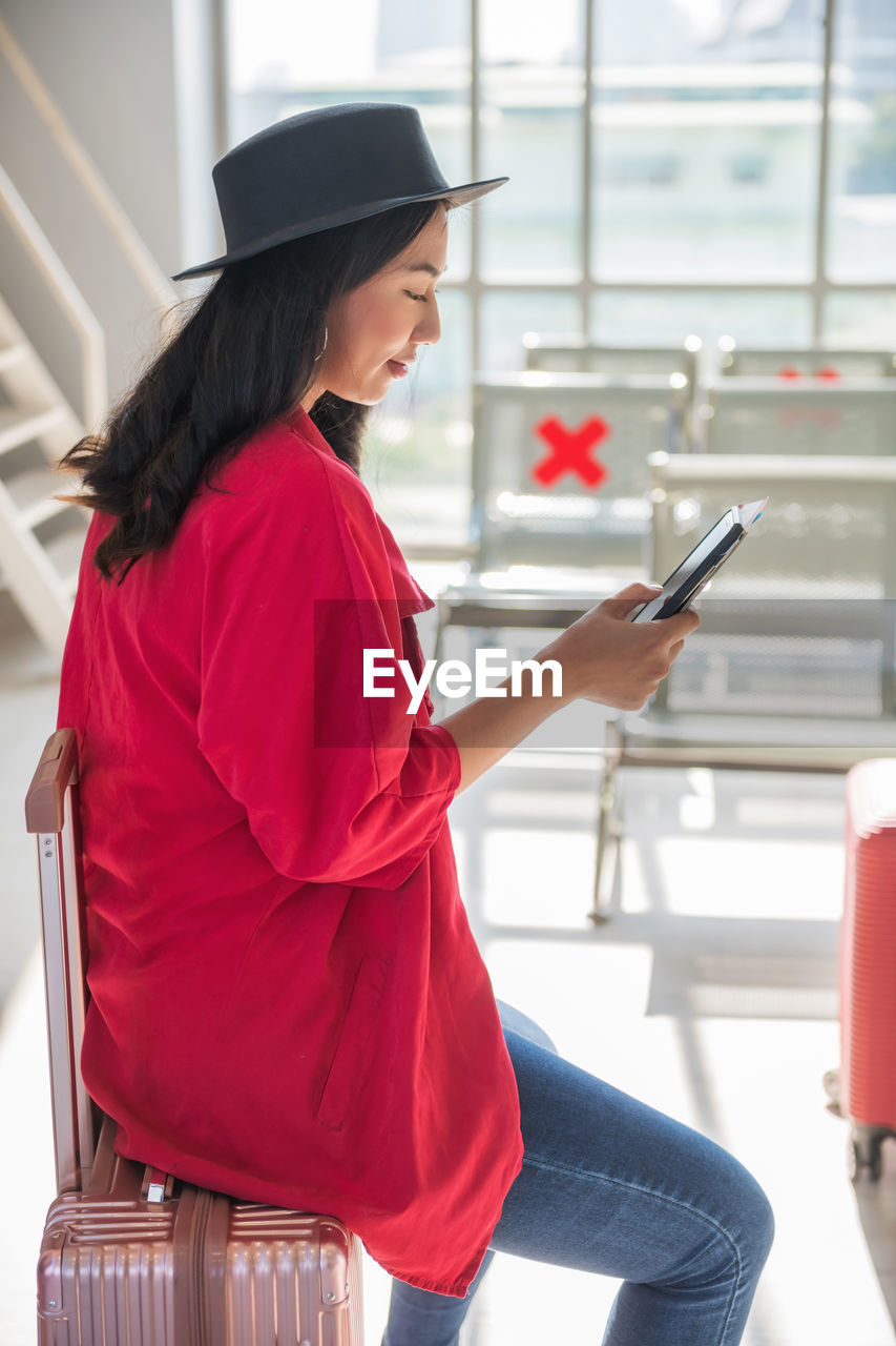 SIDE VIEW OF YOUNG WOMAN USING MOBILE PHONE IN OFFICE