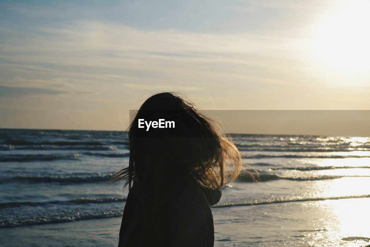 Side view of woman standing at beach against sky