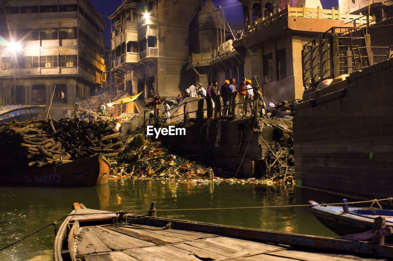 People in cremation ground next to pile of woods for burning dead bodies near ganges river