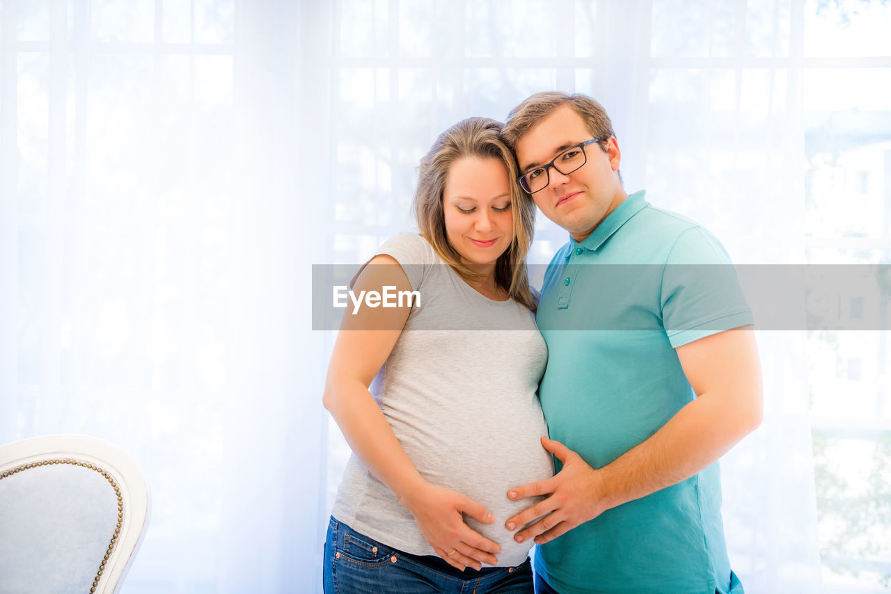 Portrait of couple standing against window