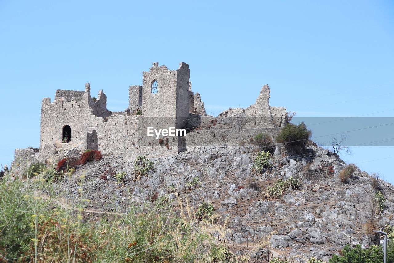 architecture, history, sky, the past, built structure, clear sky, castle, building exterior, nature, building, travel destinations, blue, plant, fort, travel, no people, old, ruins, land, ancient, medieval, old ruin, tourism, wall, day, low angle view, outdoors, fortification, sunny, tree, historic site, stone material, mountain, landscape, house, fortified wall, scenics - nature