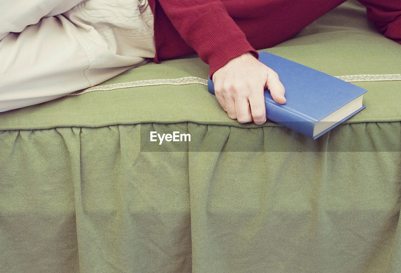 Midsection of man holding book while lying on sofa at home