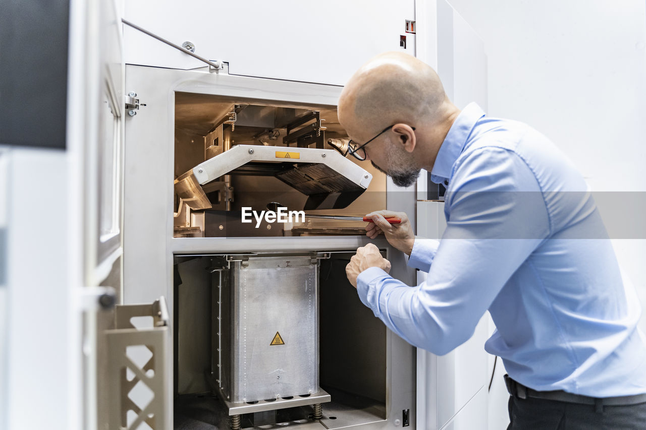 Man holding mirror examimning 3d printer