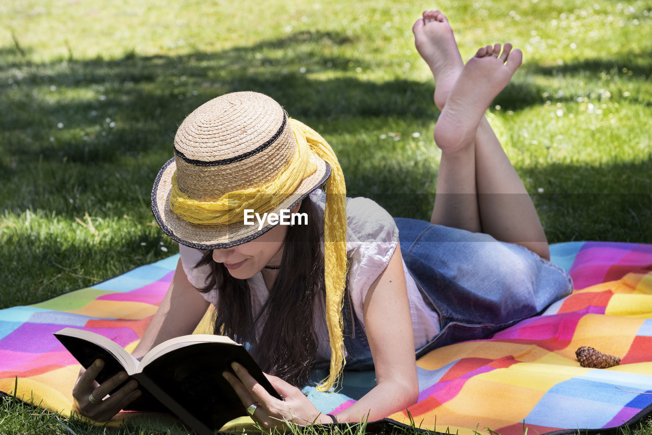 Full length of woman reading book while lying on picnic blanket in park