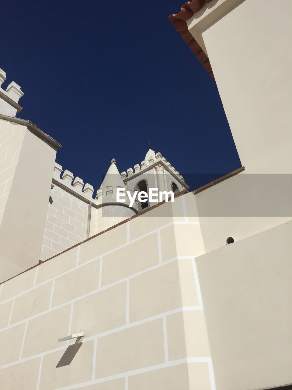 LOW ANGLE VIEW OF CROSS AMIDST BUILDINGS AGAINST CLEAR BLUE SKY