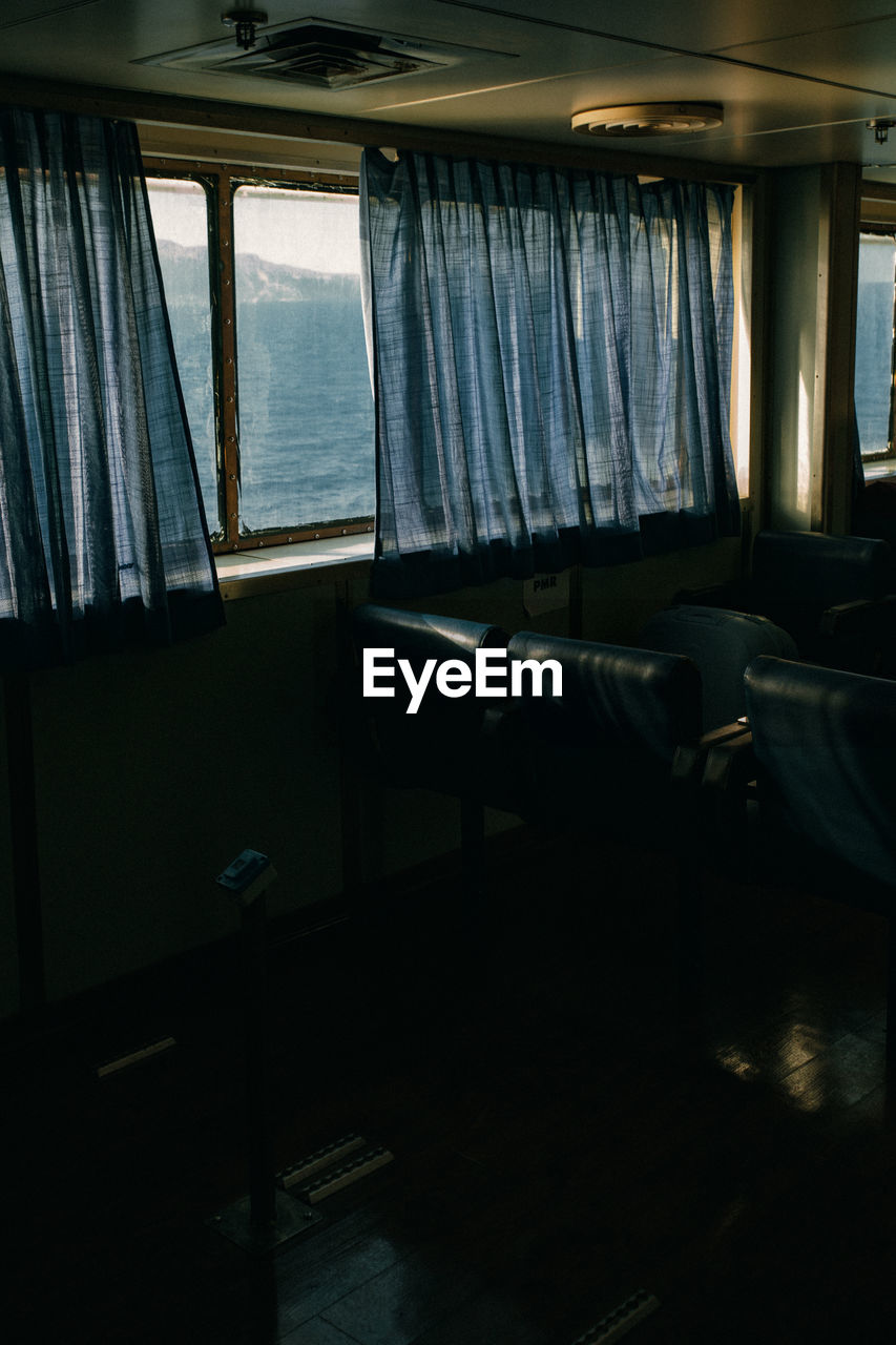 The passenger seats on the ferry boat, view through the window and curtains  behind which is sea.