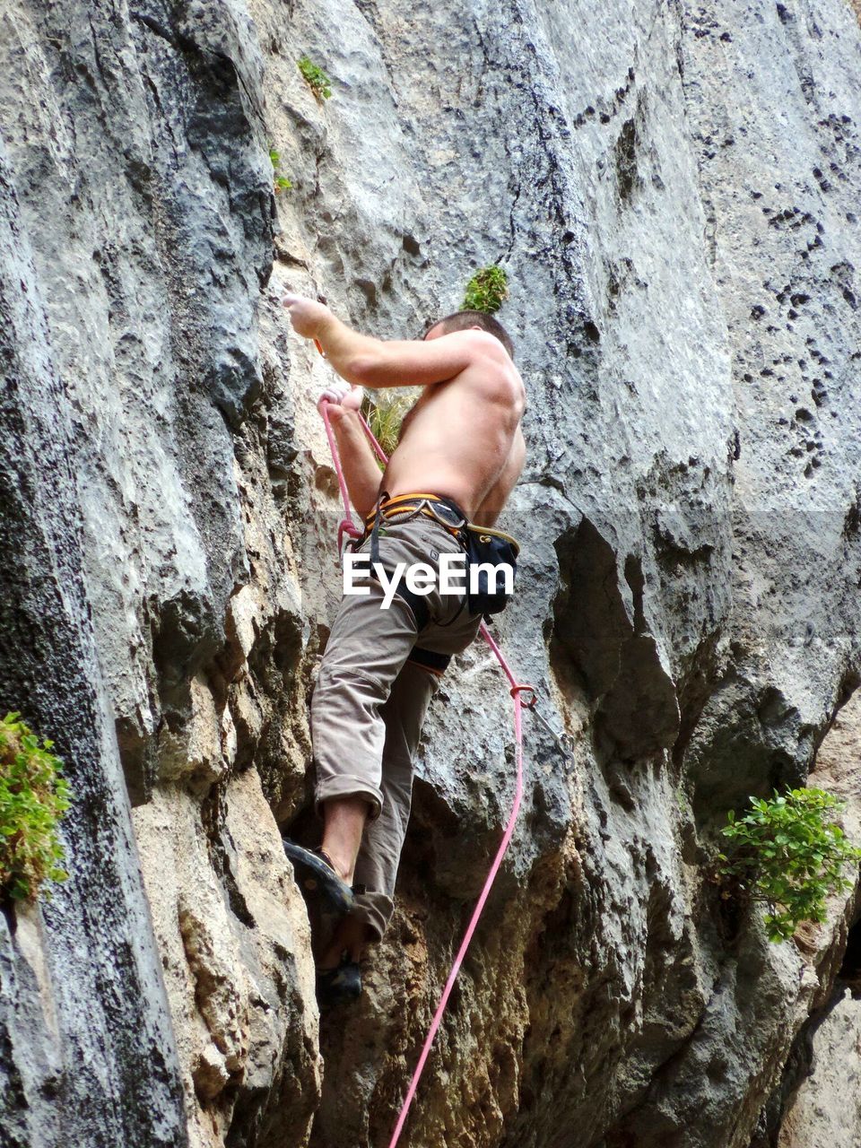Low angle view of man holding rope while climbing on rock