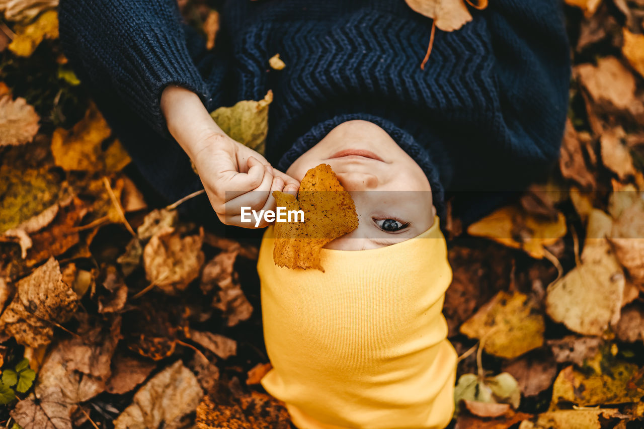 Portrait of a boy a child in a yellow hat holding an autumn leaf and lying in the fall park outdoors