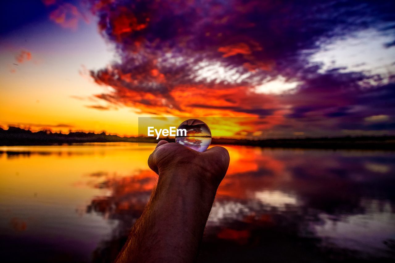 Man holding crystal ball at lake during sunset