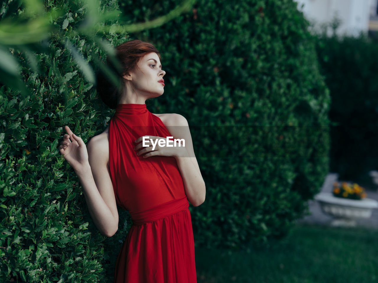 Young woman looking away while standing against plants