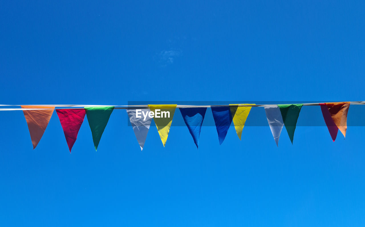 LOW ANGLE VIEW OF FLAGS HANGING AGAINST CLEAR BLUE SKY