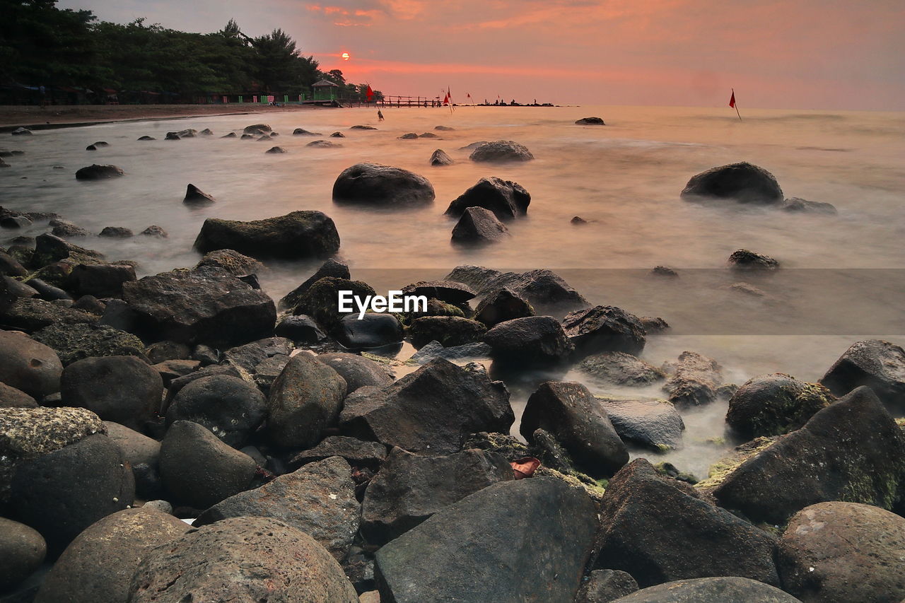 Rocks in sea against sky during sunset