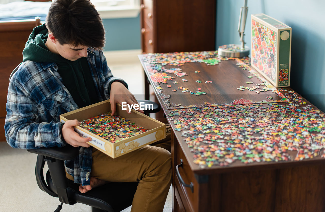 Teen boy working on a jigsaw puzzle in his bedroom during covid 19.