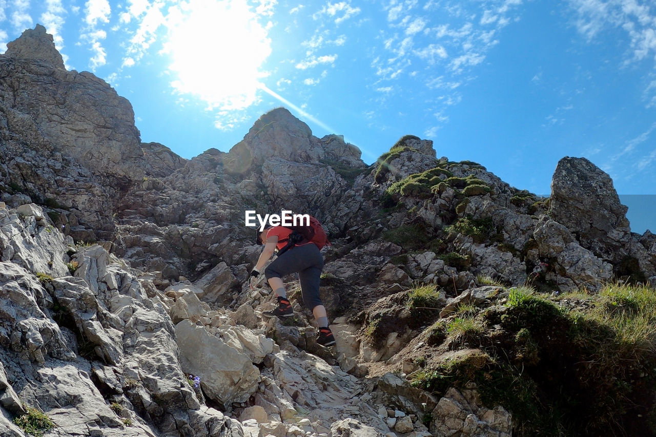 Woman climbing on rock by mountain against sky