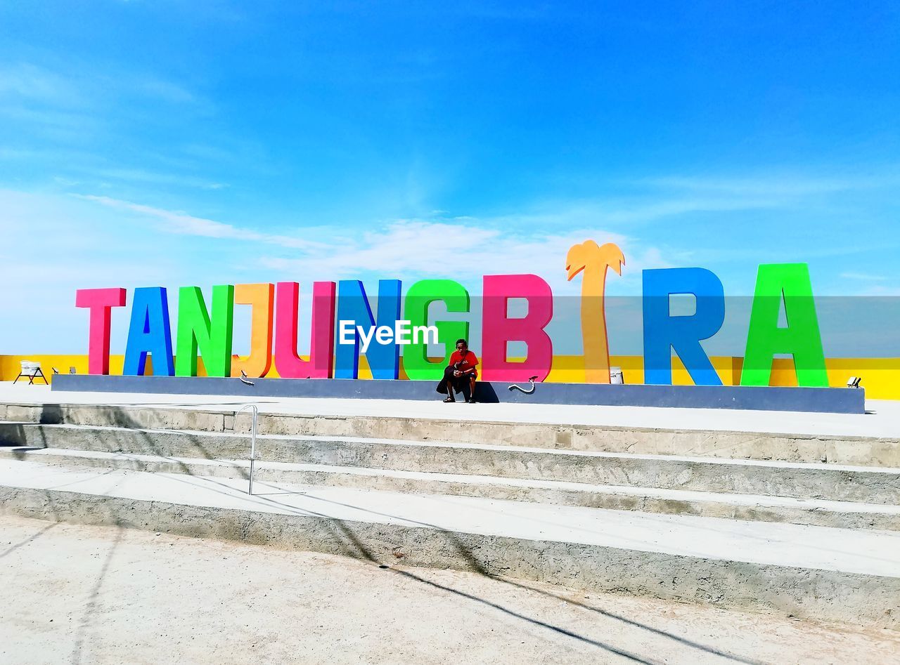 Man sitting by colorful text on steps during sunny day