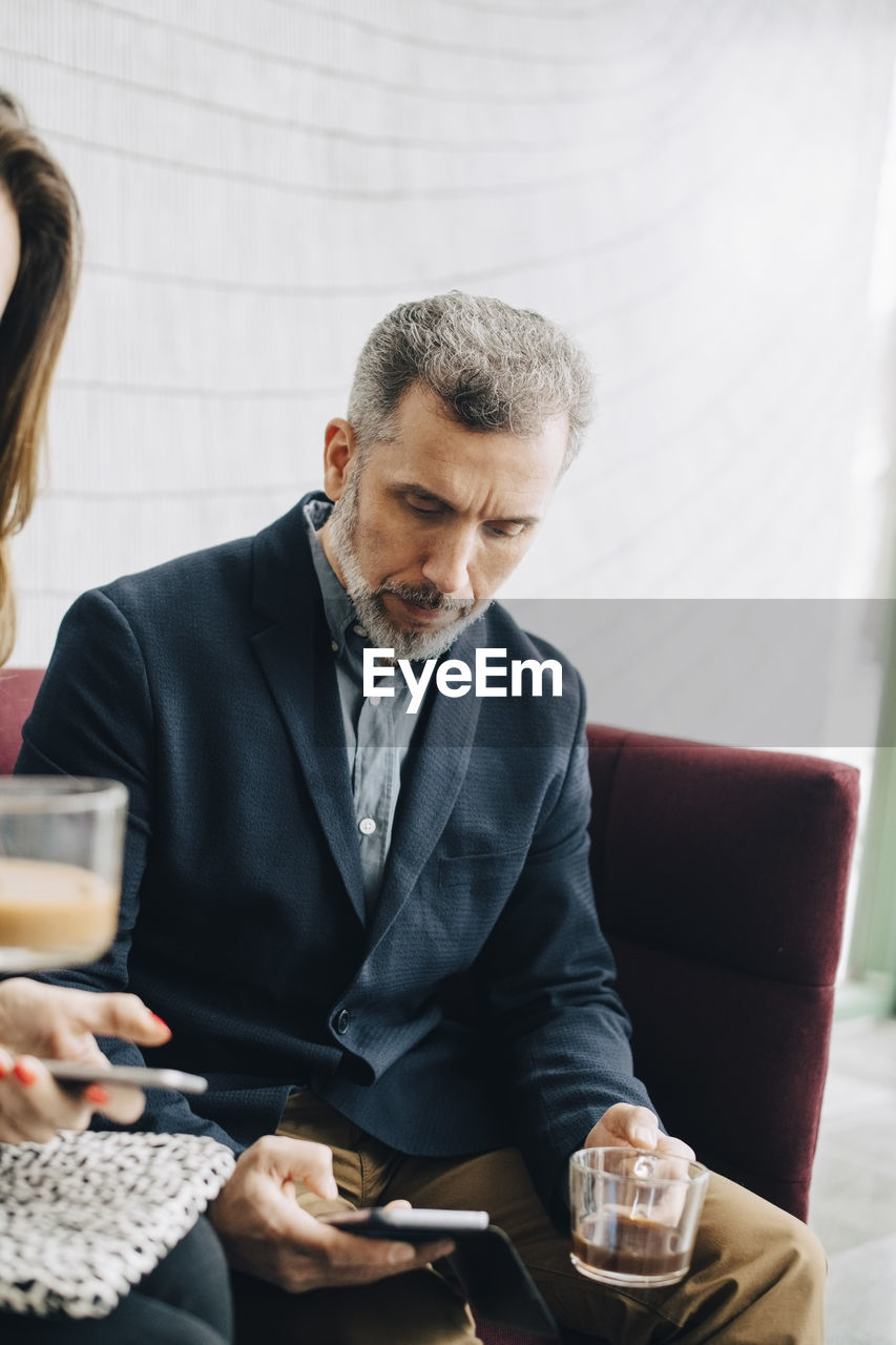 Business people using mobile phones and having drink while sitting on couch during conference