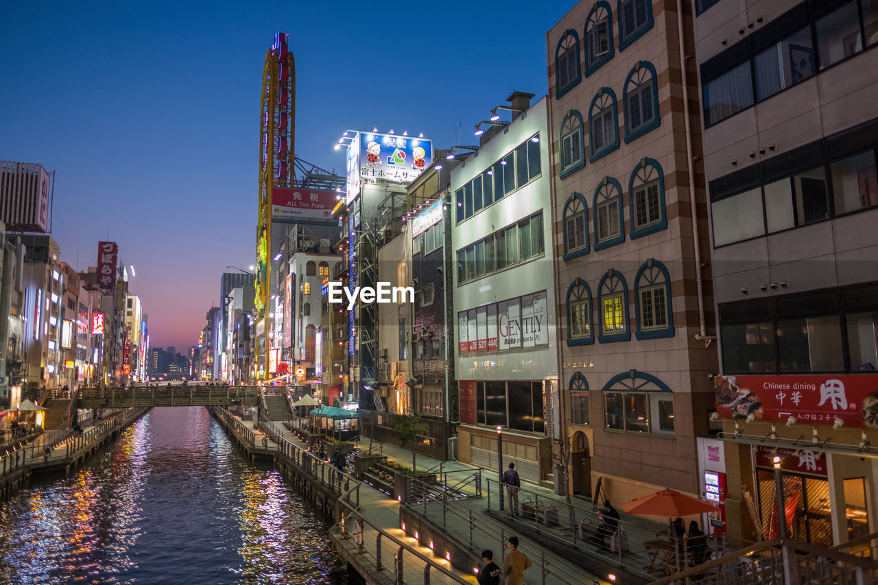 Canal amidst illuminated buildings in city during sunset