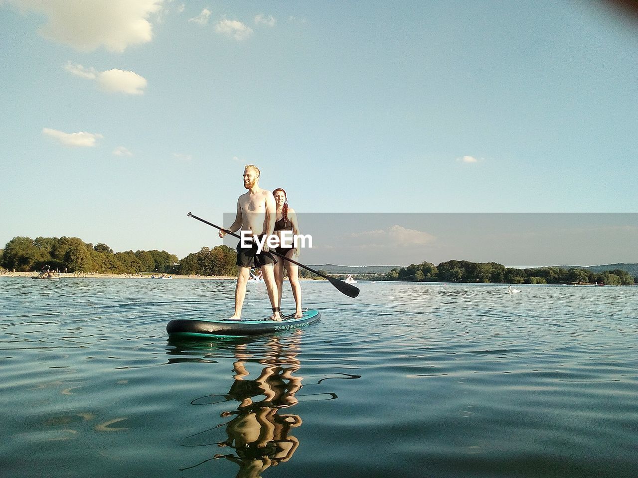 Friends standing on paddleboard in lake against sky