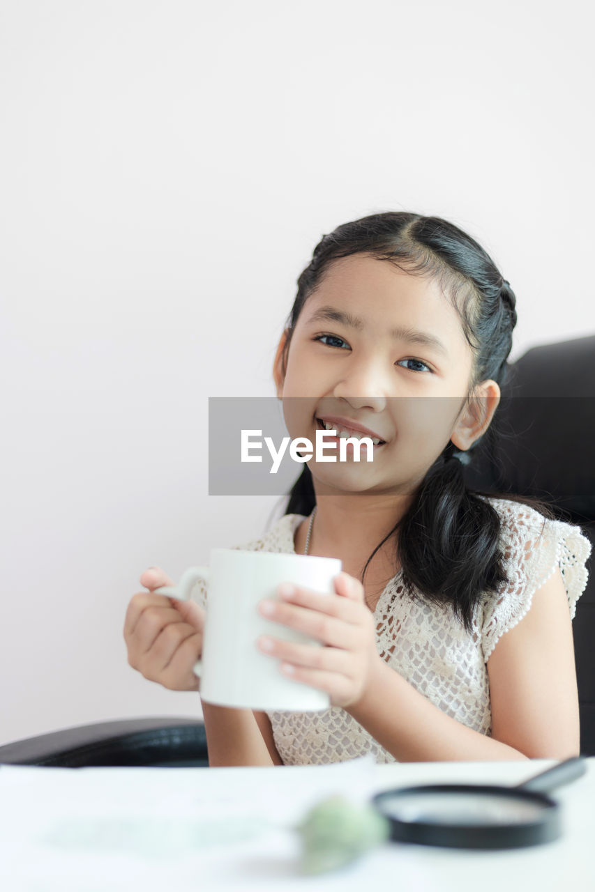 Portrait of cute girl holding mug against white background