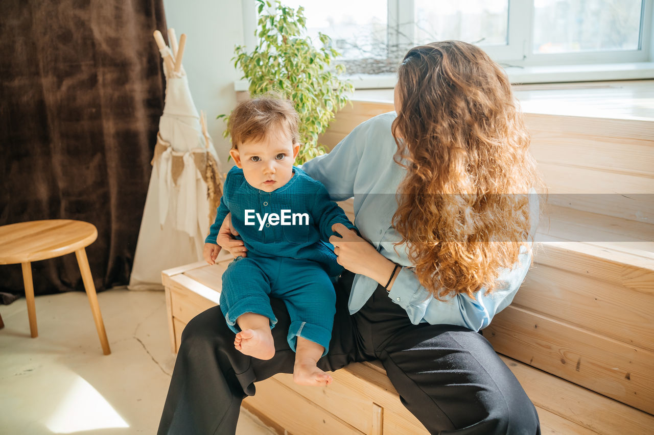 Mother with baby son on the background of a window and a wooden bench. high quality photo