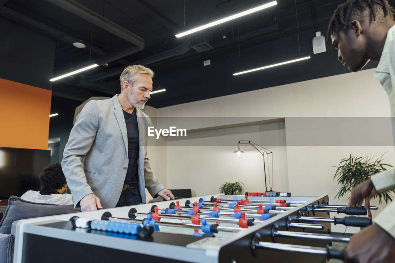 Mature businessman playing foosball with young colleague in office