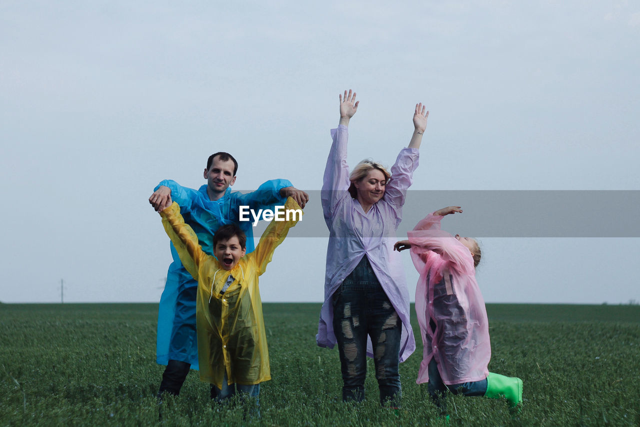 Happy family with arms raised standing on field against sky