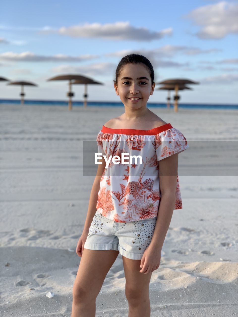 beach, one person, vacation, water, sea, land, portrait, looking at camera, childhood, child, spring, front view, standing, sand, sky, nature, smiling, day, holiday, casual clothing, leisure activity, trip, emotion, blue, three quarter length, clothing, happiness, women, female, dress, photo shoot, summer, outdoors, focus on foreground, full length, person, lifestyles, fashion, sunlight, cloud, travel destinations, travel