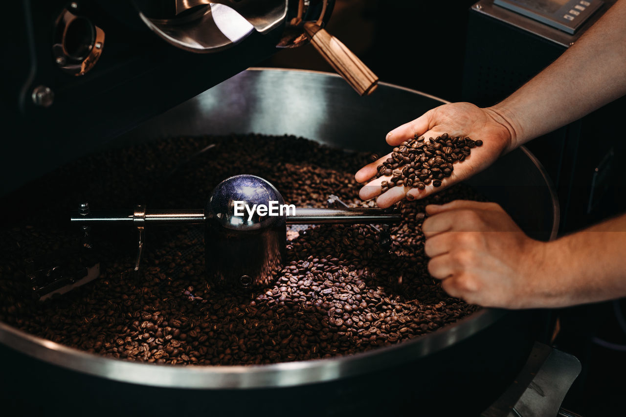 Cropped hand of man holding coffee beans over cooling rack in roaster