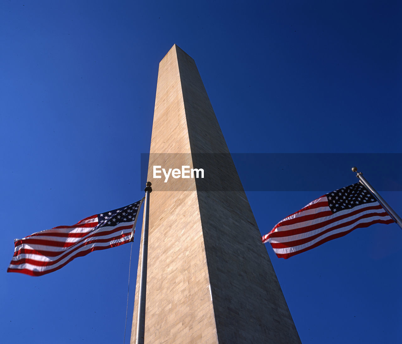 Low angle view of washington monument and american flags against clear blue sky