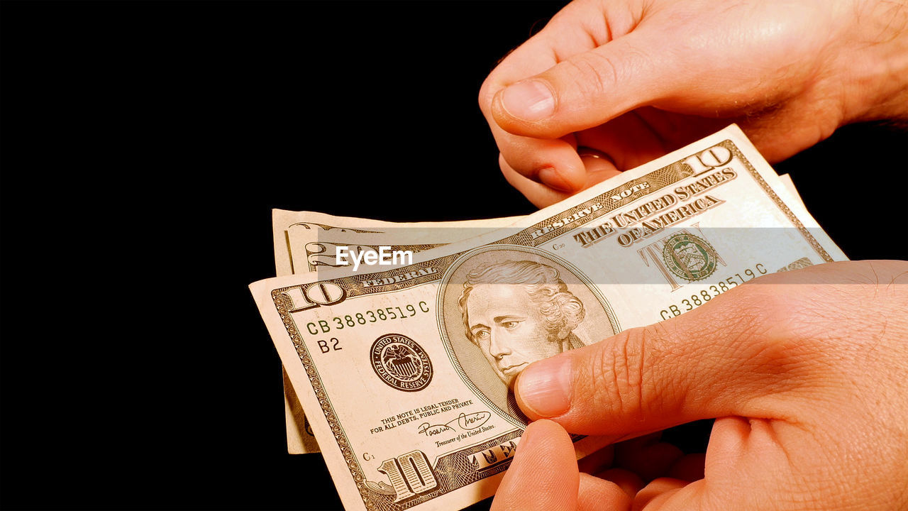 Close-up of hand holding us paper currency against black background