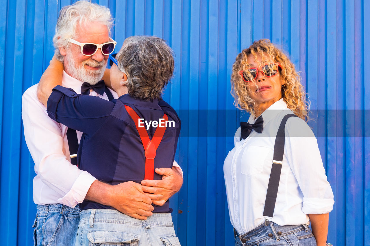 Woman standing by senior couple embracing against corrugated wall