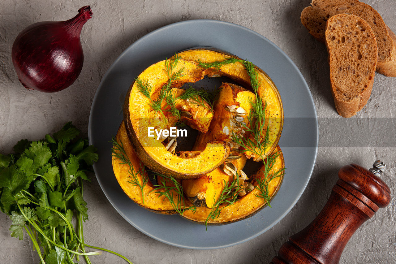 Pumpkin baked in the oven, bread, herbs, onions and spices on a gray background