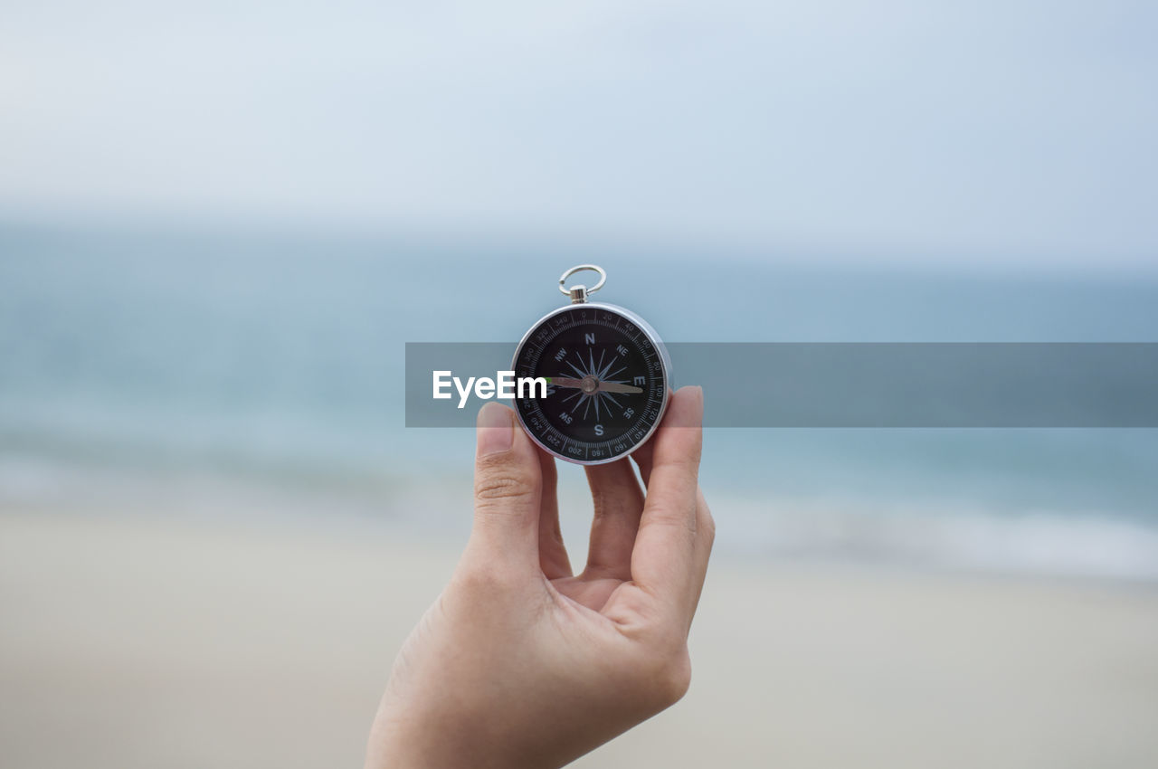 Close-up of woman holding navigational compass at beach against sky