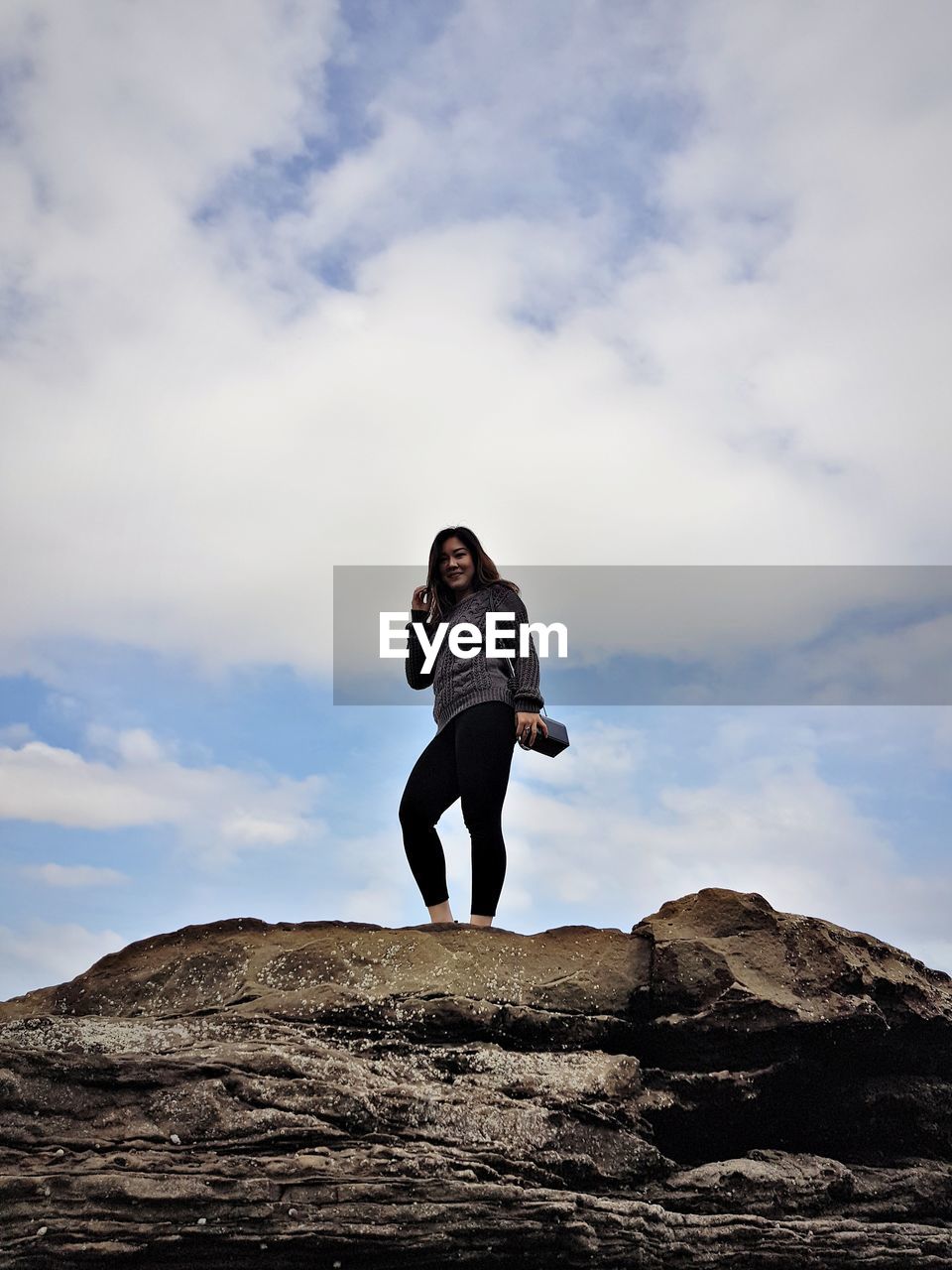 LOW ANGLE VIEW OF WOMAN STANDING ON ROCK