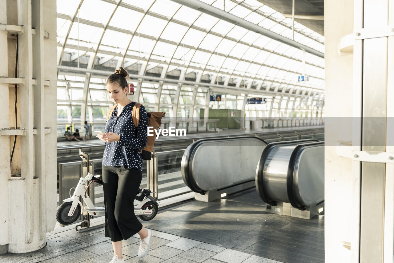 Young woman with electric scooter and cell phone at the train station