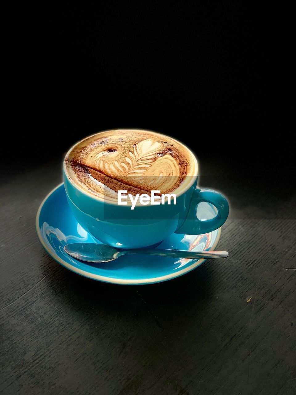 CUP OF COFFEE ON TABLE AGAINST BLACK BACKGROUND