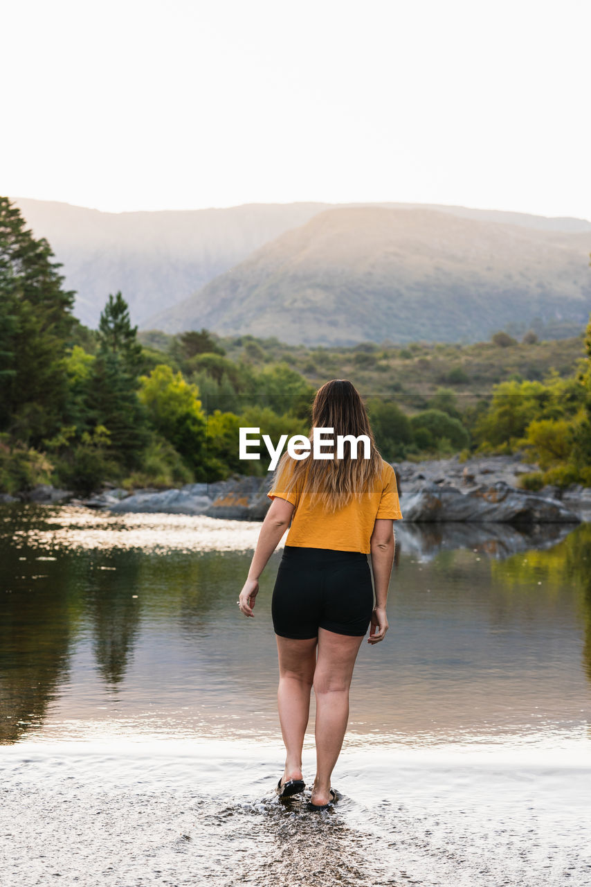 Full length rear view of woman standing by lake