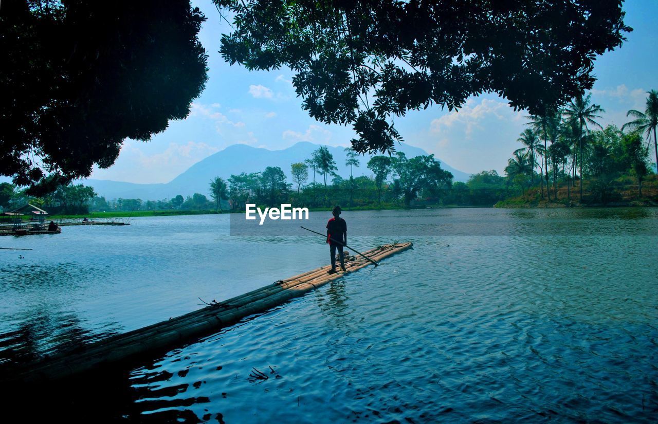 MAN STANDING IN LAKE AGAINST TREES