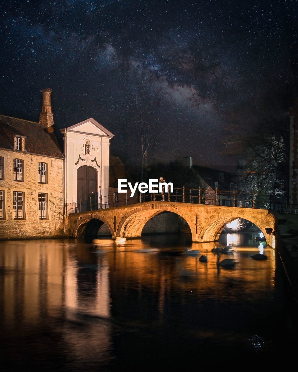 Arch bridge over river by buildings against sky at night