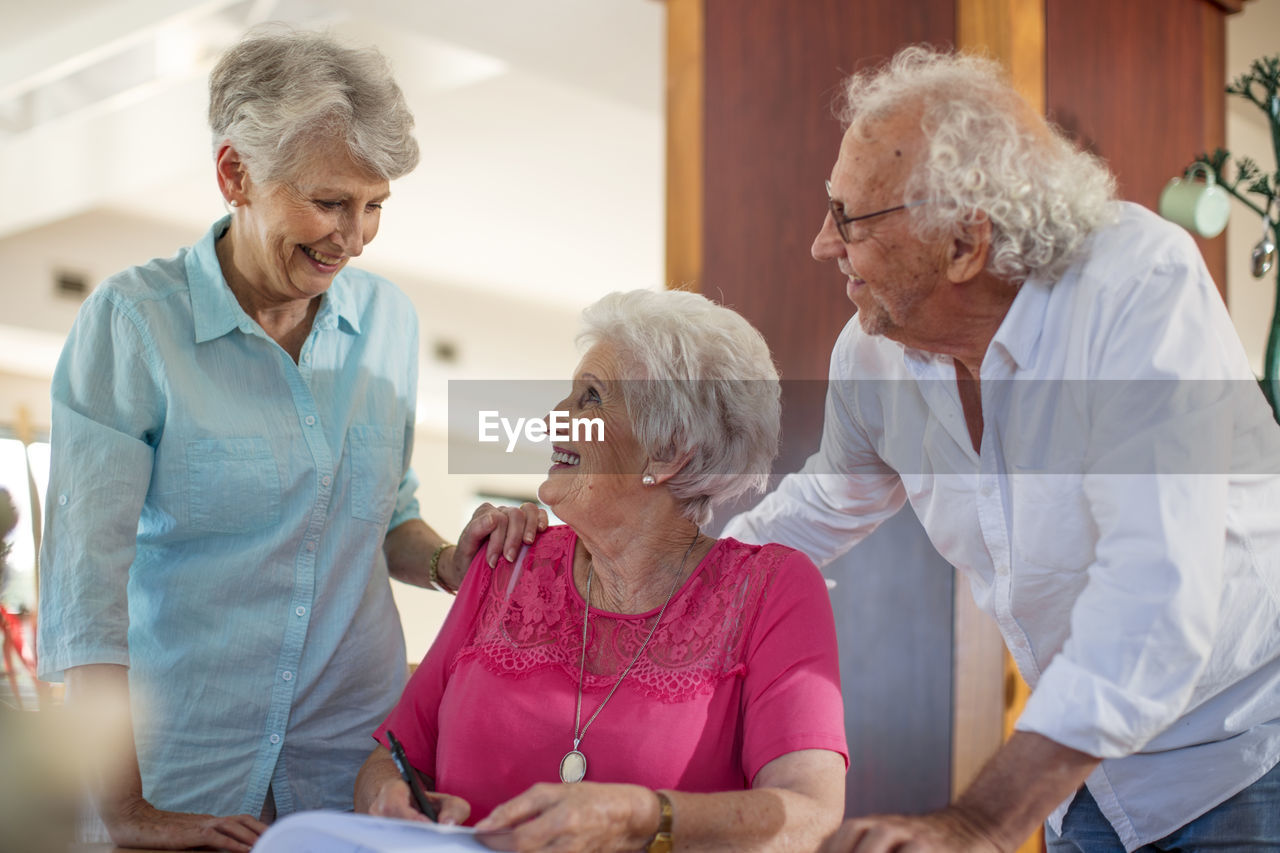 Senior woman signing a contract, friends reassuring her