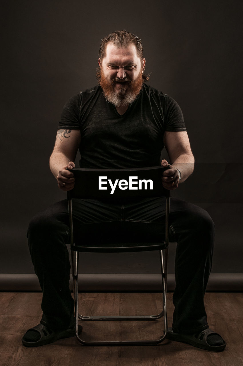 Smiling mid adult man gesturing while sitting against black background