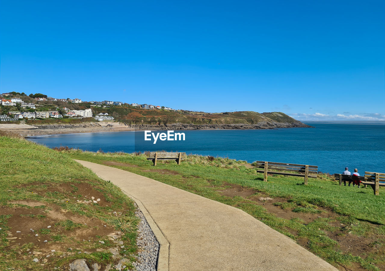 water, sea, sky, coast, land, shore, body of water, beach, nature, scenics - nature, ocean, blue, clear sky, vacation, travel destinations, beauty in nature, travel, coastline, bay, landscape, horizon, grass, tourism, cove, architecture, day, terrain, tranquility, environment, holiday, trip, tranquil scene, plant, cliff, transportation, outdoors, sunny, footpath, built structure, summer, building exterior, city, building, no people, sunlight, horizon over water, mountain, idyllic, island